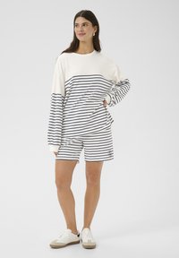 Striped pullover in cream and navy, long sleeves with ribbed cuffs, paired with matching striped shorts featuring a logo on the hem. Casual footwear.