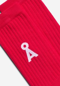 Rote gerippte Socken mit einem weißen, seitlich gestickten Logo. Die Struktur ist gestrickt und bietet ein weiches, elastisches Tragegefühl.