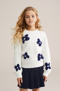 Pulover alb cu modele florale pufoase în nuanțe de navy, decolteu rotund și tiv cu volum. Asortat cu o fustă plisată din denim închis.