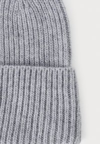 Bonnet en tricot gris avec une texture côtelée, présentant un revers replié. Le matériau semble doux et légèrement pelucheux.