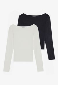 To lange ermelde gensere: en hvit og en svart, med vid halslinning og en myk, glatt tekstur. Begge har en tettsittende design.