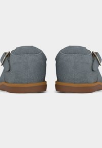 Ζευγάρι γκρι μαλακά μοκασίνια με καφέ σόλες και πλαϊνές αγκράφες, φωτογραφημένα από πίσω σε λευκό φόντο.