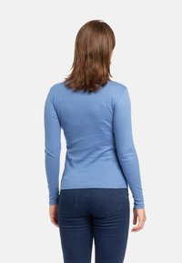 Camicia azzurra a maniche lunghe realizzata in tessuto morbido, con una vestibilità slim e una texture liscia. Abbinata a jeans in denim scuro.
