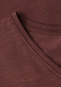 Gros plan d’un tissu brun plié montrant un tricot texturé et des coutures cousues dans un matériau doux et léger.
