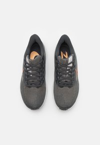 Zapatillas deportivas grises con un acento naranja, características de un upper de malla texturizada, cordones planos, cuello acolchado y un diseño de puntera redondeada.