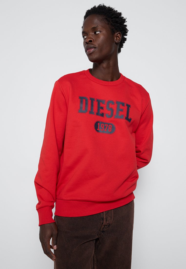 Felpa rossa in cotone con texture a costine. Presenta la scritta "DIESEL 1978" in stampa contrastante blu navy. Collo a giro e maniche lunghe.
