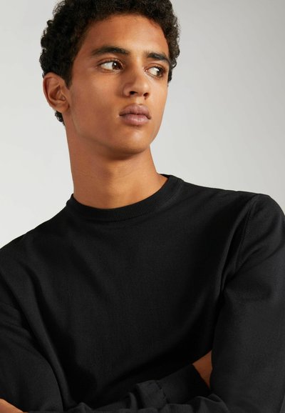 Sweatshirt noir à col rond en coton, avec des manches longues et un col à côtes, présenté sur un modèle avec des cheveux courts et bouclés.