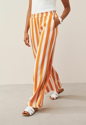 Person wearing orange and white vertical striped wide-leg pants with elastic waist, white sleeveless top, white sandals, and smartwatch.
