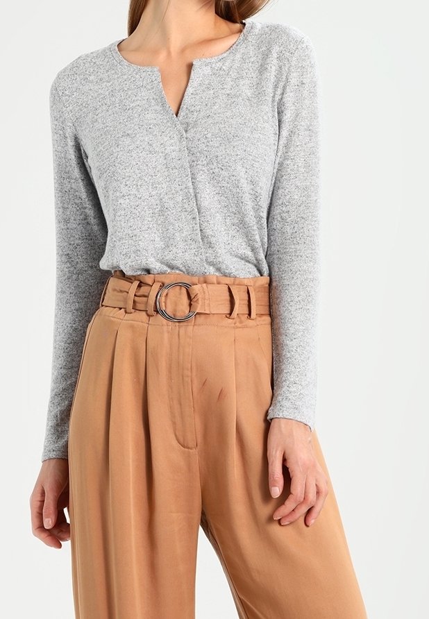 Top gris de manga larga con escote redondo, combinado con pantalones beige de cintura alta y plisados que presentan una gran hebilla de cinturón circular.