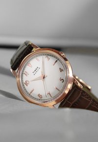 Roze gouden horloge met een witte wijzerplaat, Arabische cijfers en een brown leren band. Kenmerkt de Timex Marlin branding en een minimalistisch design.