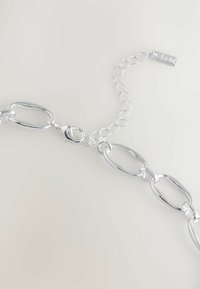 Silberne Kettenarmband mit großen ovalen Gliedern und einem Karabinerhaken, ausgestattet mit einer verstellbaren Verlängerungskette und einem rechteckigen Anhänger.