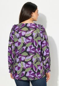 Blusa a maniche lunghe con un motivo floreale in nero, verde e viola. Accenti a volant sulle spalle e polsini elasticizzati.