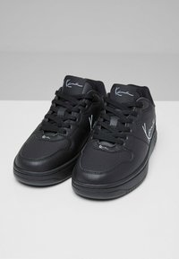 Schwarze Sneakers aus Leder mit glatter Textur, runden Zehen, flacher Sohle und Schnürsenkeln. Weiße Logoakzente an den Seiten.