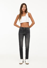 Jeans neri slim-fit con vita media, denim leggero e dettagli strappati. Abbinati a un top corto bianco e scarpe da ginnastica.