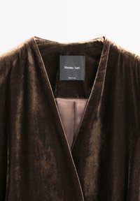 Brunt fløjlsplagg med dyb V-udskæring og en glat inderside. Har et mærke med teksten "Massimo Dutti." Blød tekstur med let glans.