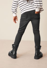 Jean skinny noir avec poches arrière, associé à des bottines en cuir noires à la cheville avec une boucle, porté avec une chemise à rayures à manches longues.