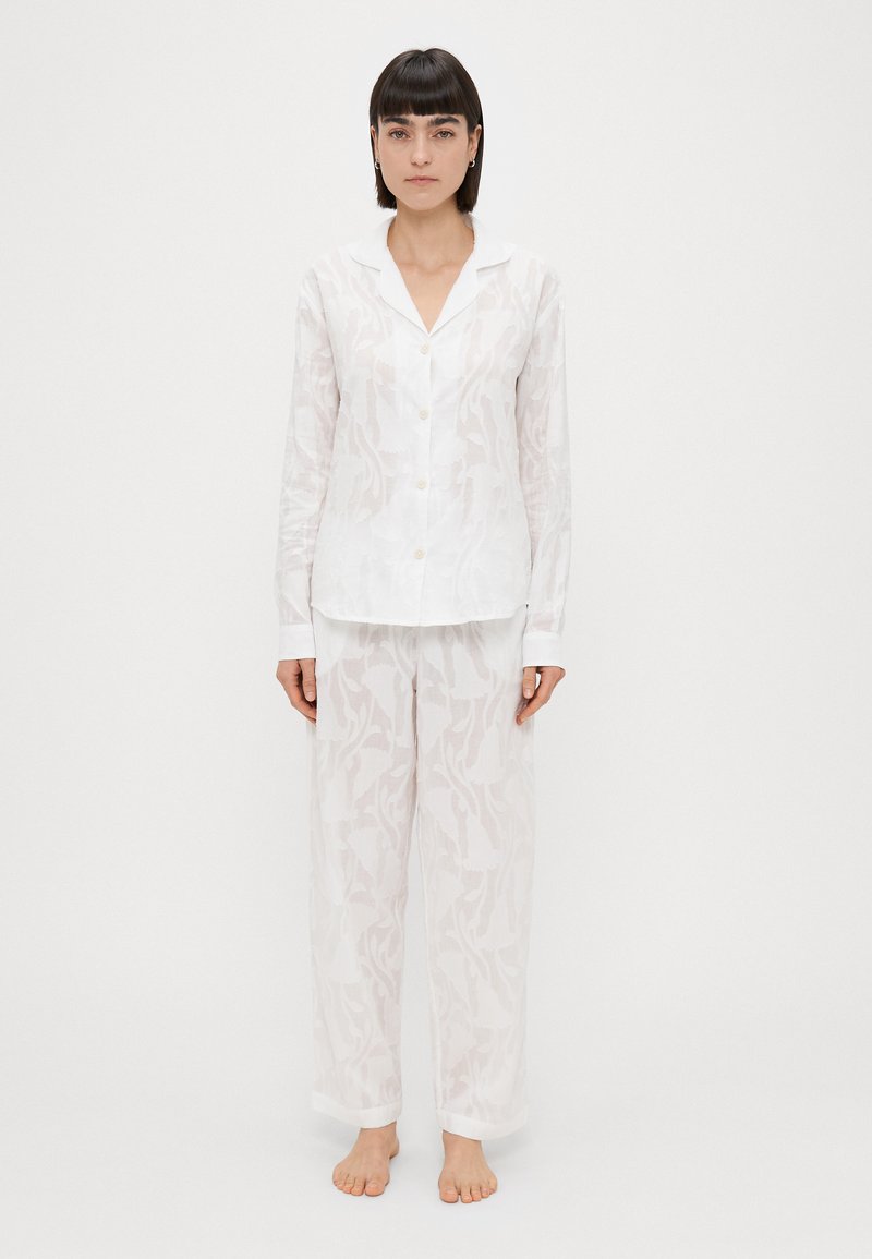 Biele, ľahké pyžamo pozostávajúce z goliera, košele na gombíky a voľných nohavíc s jemným kvetinovým vzorom. Mäkká textúra.