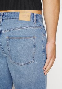 Světle modré džíny z denimu se střihem rovného střihu. Mají koženou značkovou etiketu, zadní kapsu a viditelné švy.