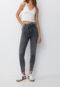 Szare, wysokim stanem, obcisłe jeansy o gładkiej fakturze; zestawione z białym, prążkowanym crop topem z falistymi krawędziami i cienkimi ramiączkami.