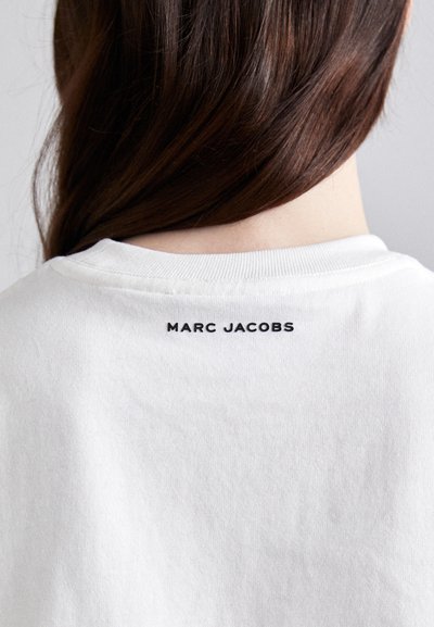 White cotton t-shirt featuring a crew neck and short sleeves, with "MARC JACOBS" printed in black at the back neckline.
