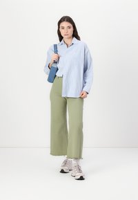 Camicia button-up a righe blu chiaro, pantaloni a gamba larga verde oliva e sneakers grigie. Gli accessori includono una borsa di jeans. Look pulito e casual.