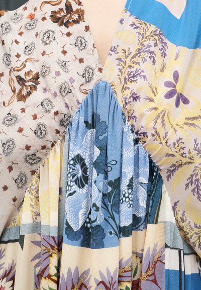 Gros plan d'une robe patchwork multicolore avec des motifs floraux dans des tons beige, bleu, violet et jaune avec des détails en tissu plissé.
