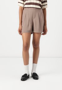 Shorts en lin marron avec des plis, longueur mi-cuisse, associés à des chaussettes blanches côtelées et des mocassins noirs. Haut en tricot rayé visible au-dessus.