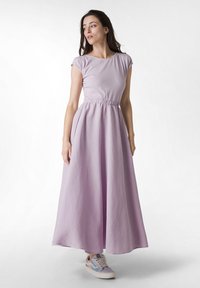 Rochie maxi fără mâneci, de culoare lavandă, cu talie strânsă și buzunare pe lateral, asortată cu pantofi sport casual. Material neted și design fluid.