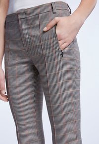 Pantalon à carreaux avec un motif à carreaux noir, blanc et rouge, coupe slim, poches latérales, fabriqué en tissu texturé.