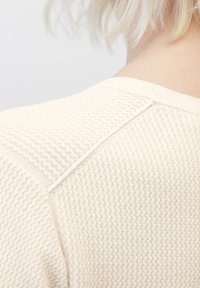 Pull en maille texturée crème avec un motif en zigzag distinctif, doté d'un col côtelé et d'un détail de couture à l'épaule.