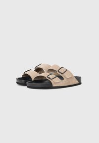 Beige semskede sandaler med to justerbare sorte spenner, svart gummisåle og åpen tå-design for komfort og pusteevne.