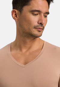 Beżowa koszulka z dekoltem w serek, wykonana z gładkiego, miękkiego materiału. Dopasowany krój z krótkimi rękawami i czystym dekoltem. Subtelna tekstura.