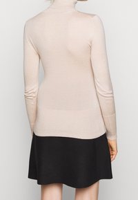 Hellrosa Rollkragenpullover aus feiner Strickware, kombiniert mit einem schwarzen ausgestellten Rock, von hinten betrachtet. Glatte Textur, figurschmeichelnde Passform.