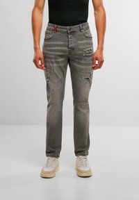 Jeanși din denim gri, cu croială dreaptă, având detalii uzate, un accent roșu la talie și stropi subtili de vopsea albastră.