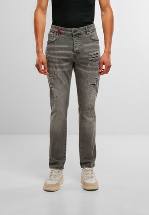 Jean en denim gris avec une coupe droite, affichant des détails usés, un accent rouge à la taille et de légères éclaboussures de peinture bleue.