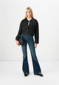 Svart cropped jakke med knappelukking og to frontlommer, parret med bredde blå jeans og en liten svart håndveske.