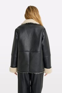 Giubbotto in pelle nera con colletto e polsini in montone, caratterizzato da una vestibilità comoda e dettagli delle cuciture visibili sul retro.
