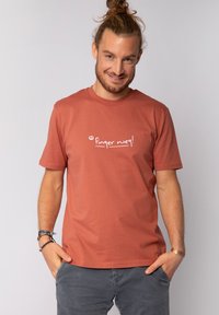 Rostfarbendes Baumwoll-T-Shirt mit kurzen Ärmeln und Rundhalsausschnitt; mit weißem Text "Finger weg!" auf der Brust bedruckt.