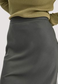 Grauer Bleistiftrock mit glatter Textur und taillierter Silhouette, kombiniert mit einem gerippten olivgrünen Pullover in der Taille.