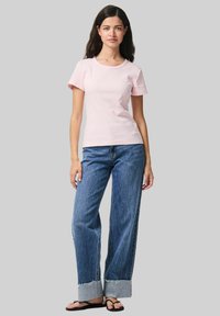 Gaiši rozā īsām piedurknēm T-krekls ar apaļu kaklu, kopā ar platām zilu džinsu biksēm ar saplēstu apakšmalu un kontrastējošu apkakli.