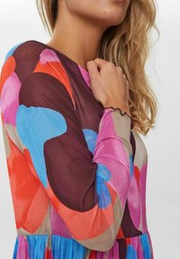 Färggad långärmad topp med djärva abstrakta mönster i rosa, orange, blått och brunt. Mjuk, transparent tyg med volangdetalj vid nederkanten.