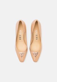 Decolté in vernice beige con punta affusolata e un accento triangolare in argento sul davanti. Texture liscia.