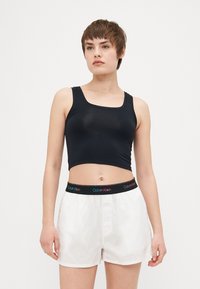Svart cropped linne med fyrkantig halsringning, matchat med vita shorts som har ett flerfärgat Calvin Klein-logoband i midjan.