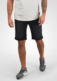 Shorts en denim foncé avec des ourlets retroussés, présentant des détails usés à l'avant. Associés à des chaussures de sport grises et un t-shirt gris clair.