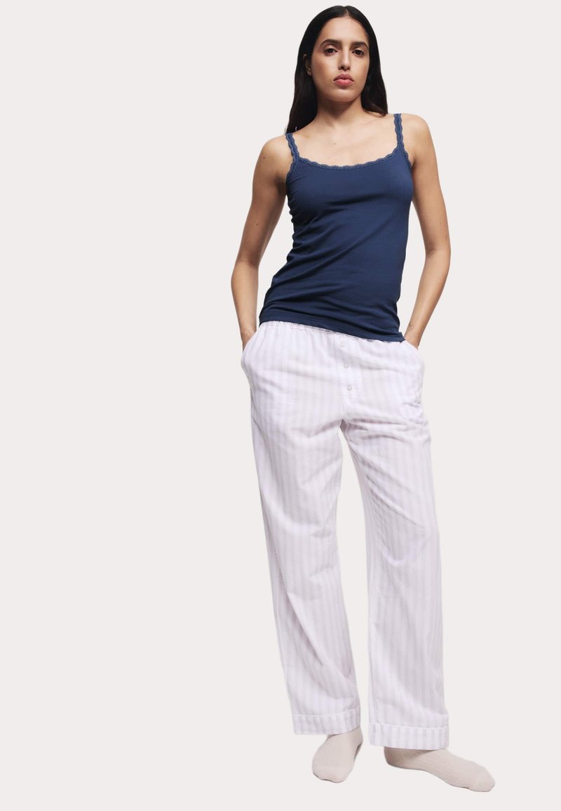 Top in cotone navy con bordo in pizzo e pantaloni da pigiama bianchi a righe. I pantaloni presentano una chiusura con bottone e tasche laterali.