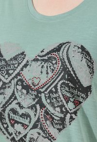 Lys grøn skjorte med sorte hjerteformede ingefærkager og røde rhinestones på brystområdet.