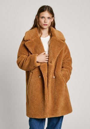 Bruine oversized nepleren bontjas met grote notch revers, dubbele knoopsluiting, zijzakken en een zachte, textuurafwerking.