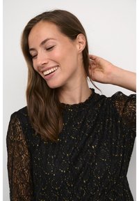 Svart spetsklänning med ett virvlande mönster och metallic guld-accenter. Hög halsringning och långa ärmar med texturerad detalj.