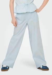 Pantalons larges bleu clair avec une texture douce et une coupe décontractée, associés à des baskets navy avec des accents blancs et beige.