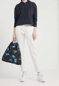 Marinblå hoodie med en текстurerad logotyp, vita skräddarsydda byxor och en svart blommig dragsko-väska med blå blommor. Vita sneakers fulländar outfiten.